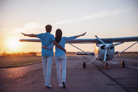Back view of beautiful romantic couple hugging while walking on take-off ground near the aircraftの写真素材