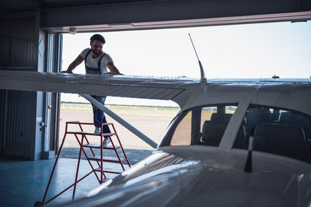 Handsome bearded mechanic in uniform is smiling while cleaning the aircraft in hangarの写真素材
