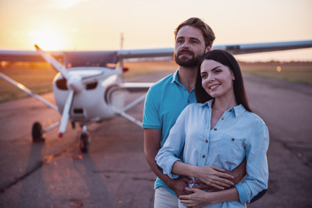 Beautiful romantic couple is hugging and smiling while enjoying the view on take-off ground near the aircraftの写真素材
