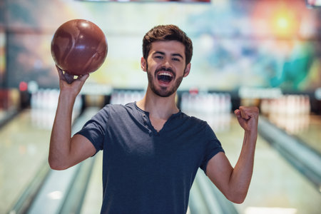 Handsome guy is holding a bowling ball, looking at camera and smiling ready to play bowlingの写真素材