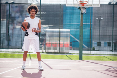 Full length of attractive basketball player holding a ball while playing on basketball court outdoorsの写真素材