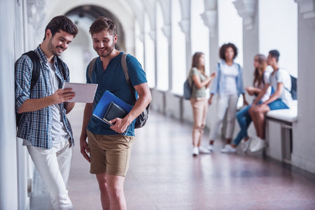 Beautiful young students are resting in university hall, a guys in the foreground are using a digital tablet and smilingの写真素材