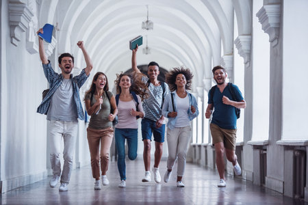 Beautiful young students are looking at camera and smiling while running through the university hallの写真素材