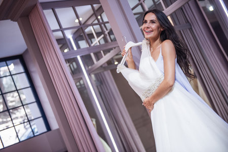 Beautiful young bride is smiling while choosing elegant wedding dresses in modern wedding salonの写真素材