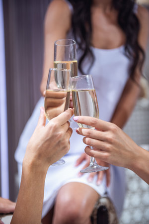 Cropped image of bride in elegant wedding dress and her friends clinking glasses of champagne while visiting modern wedding salonの写真素材