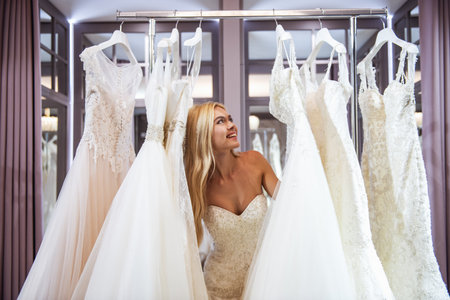 Attractive young bride is smiling while choosing wedding dress in modern wedding salonの写真素材