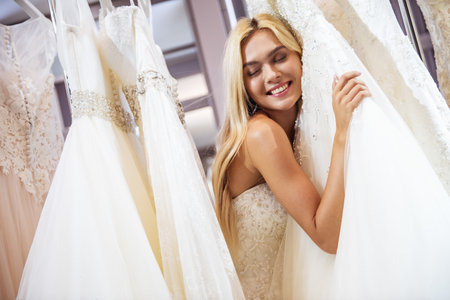 Attractive young bride is smiling while choosing wedding dress in modern wedding salonの写真素材