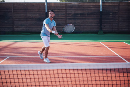 Handsome man is playing tennis on tennis court outdoorsの写真素材