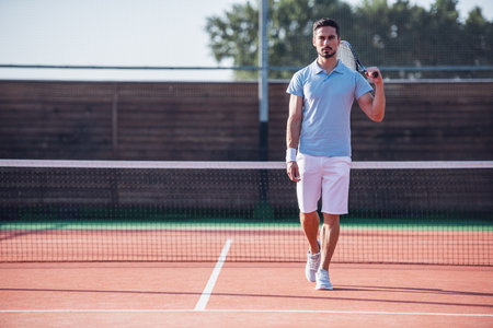 Handsome man is holding tennis racket while playing tennis on court outdoorsの写真素材
