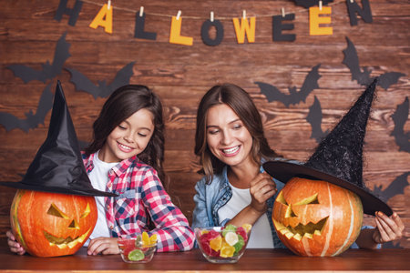 Cute little girl and her beautiful mom are smiling while preparing pumpkins for Halloweenの写真素材