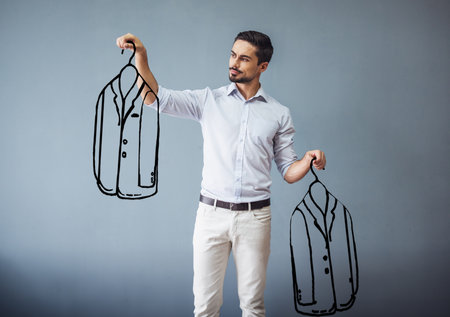 Handsome man in smart casual wear is holding drawn men suits and choosing between, on gray backgroundの写真素材