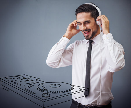 Handsome businessman in classic suit, sun glasses and headphones is making music with drawn dj panel, on gray backgroundの写真素材