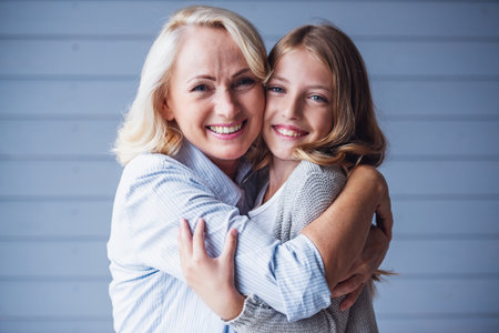 Beautiful granny and  teenage granddaughter are hugging, looking at camera and smilingの写真素材