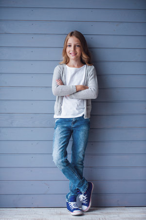 Beautiful teenage girl smiling while standing with crossed arms against a wooden wall backgroundの写真素材
