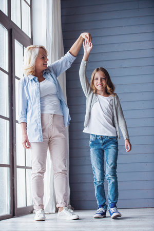 Beautiful granny and  teenage granddaughter are holding hands and smiling while spending time together at homeの写真素材