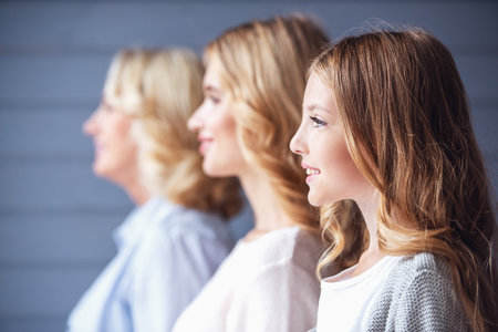 Side view of beautiful women generation: granny, mom and daughter smiling while standing in a rowの写真素材
