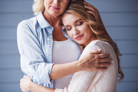 Beautiful senior mom and her adult daughter are hugging and smilingの写真素材