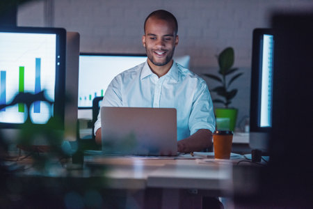 Handsome Afro American businessman in classic suit is using a laptop and smiling while working in office late at nightの写真素材