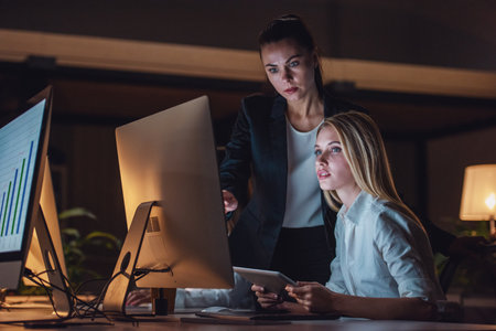 Beautiful business women are using a computer while working in office late in the eveningの写真素材
