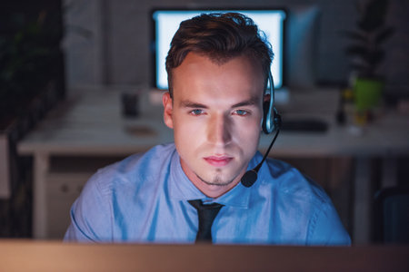 Handsome businessman in headset is working with a computer in office late at nightの写真素材