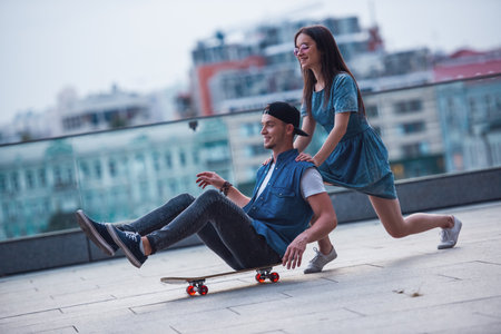 Young couple is having fun outdoors, girl is pushing her boyfriend on a skateboardの写真素材