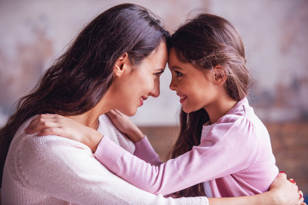 Beautiful mom and daughter are hugging, touching with their headphones and smilingの写真素材