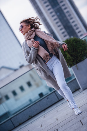 Beautiful girl in coat and sun glasses is walking outdoorsの写真素材