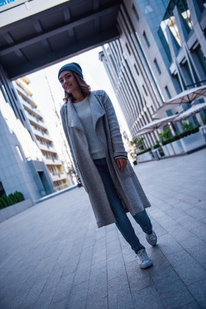 Full length image of beautiful girl in coat and cap smiling while walking in the cityの写真素材