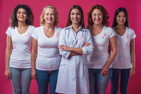 Women against breast cancer. Beautiful women of different ages and nationalities with pink ribbons on their chests are looking at camera and smiling, on red backgroundの写真素材