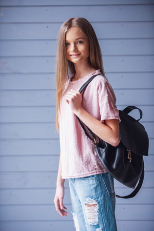 Attractive teenage girl with backpack looking at camera and smiling against wooden wall backgroundの写真素材