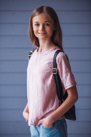 Attractive teenage girl with backpack looking at camera and smiling against wooden wall backgroundの写真素材