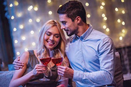 Beautiful young couple is hugging, drinking wine and smiling during their date in a restaurantの写真素材