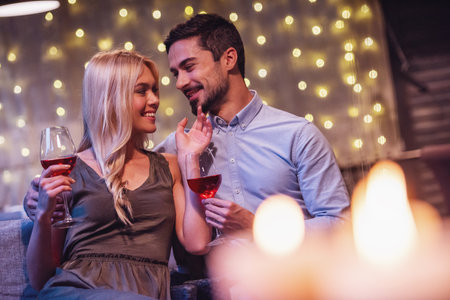 Beautiful young couple is looking at each other, drinking wine and smiling during their date in a restaurantの写真素材