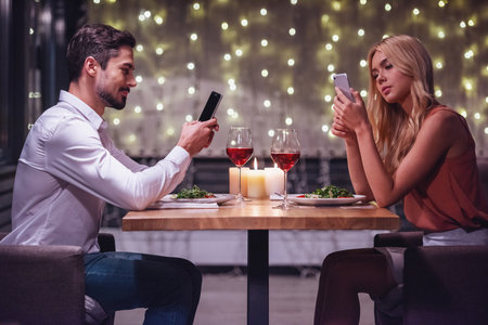 Young couple is using in their smartphones during their date in a restaurantの写真素材