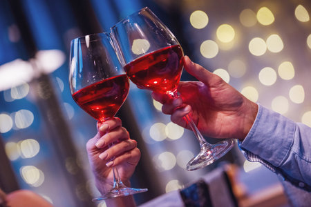 Cropped image of couple clinking glasses of wine together while having a date in a restaurantの写真素材