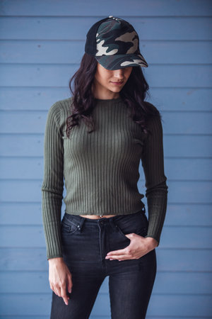 Attractive young woman in camouflage cap is posing at camera, on gray backgroundの写真素材