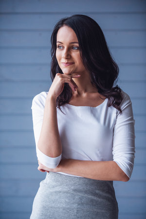 Attractive young woman is looking away and smiling, on gray backgroundの写真素材