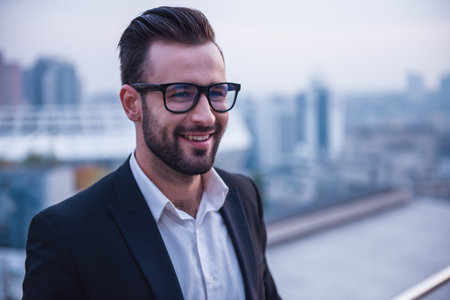 Handsome businessman in suit and glasses is smiling while standing on the balconyの写真素材