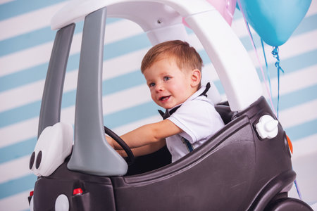 Cute little boy is smiling while sitting in the toy car, on light backgroundの写真素材