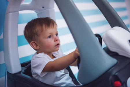 Cute little boy is very serious while sitting in the toy carの写真素材