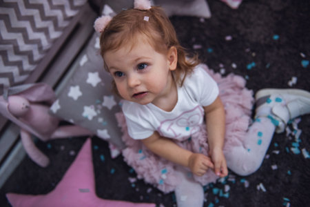 Cute little girl is playing with confetti in the children's roomの写真素材