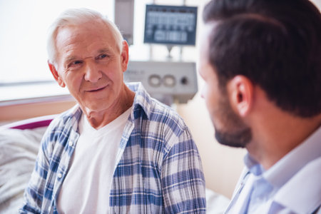 Handsome old man is talking with a doctor while sitting in hospital wardの写真素材