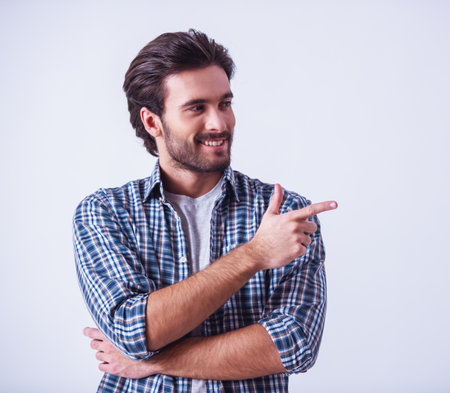Handsome bearded man in casual clothes is pointing away and smiling, on light backgroundの写真素材