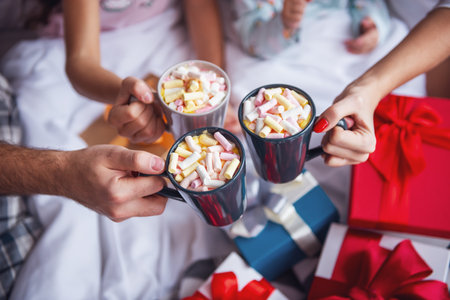 It's Christmas time! Cropped image of parents and their daughter holding cups while sitting in bed with presentsの写真素材