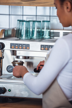 Beautiful Afro American barista in apron is preparing coffee using a coffee machineの写真素材