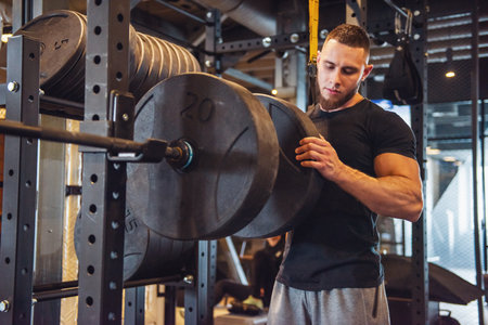 A young strong man adds weight to his barbell while training in the gym.の写真素材