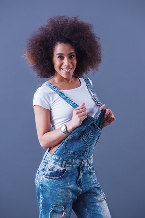 Beautiful woman in jean overalls is smiling, on a grey backgroundの写真素材