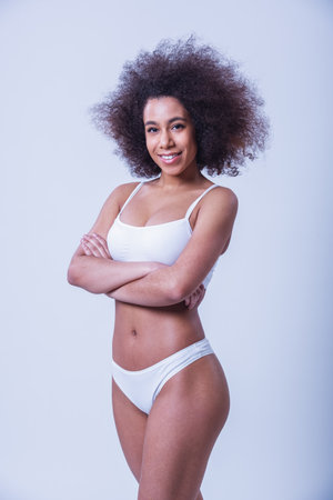 Beautiful woman in white lingerie is posing and smiling at camera, on a grey backgroundの写真素材