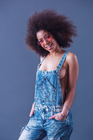 Beautiful woman in jean overalls is posing at camera and smiling, on a grey backgroundの写真素材