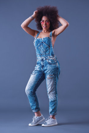 Beautiful woman in jean overalls is posing at camera and smiling, on a grey background, full-lengthの写真素材